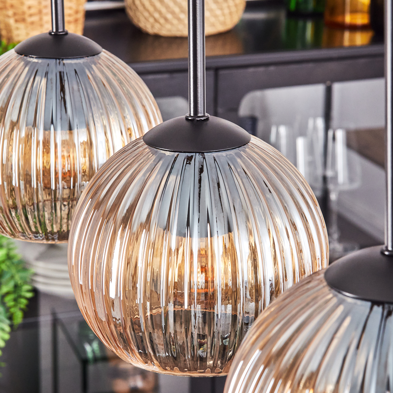 Drei Pendelleuchten aus Glas. Jede hat ein geripptes Design und hängt an schwarzen Metallstangen. Im Hintergrund sind Küchenelemente.