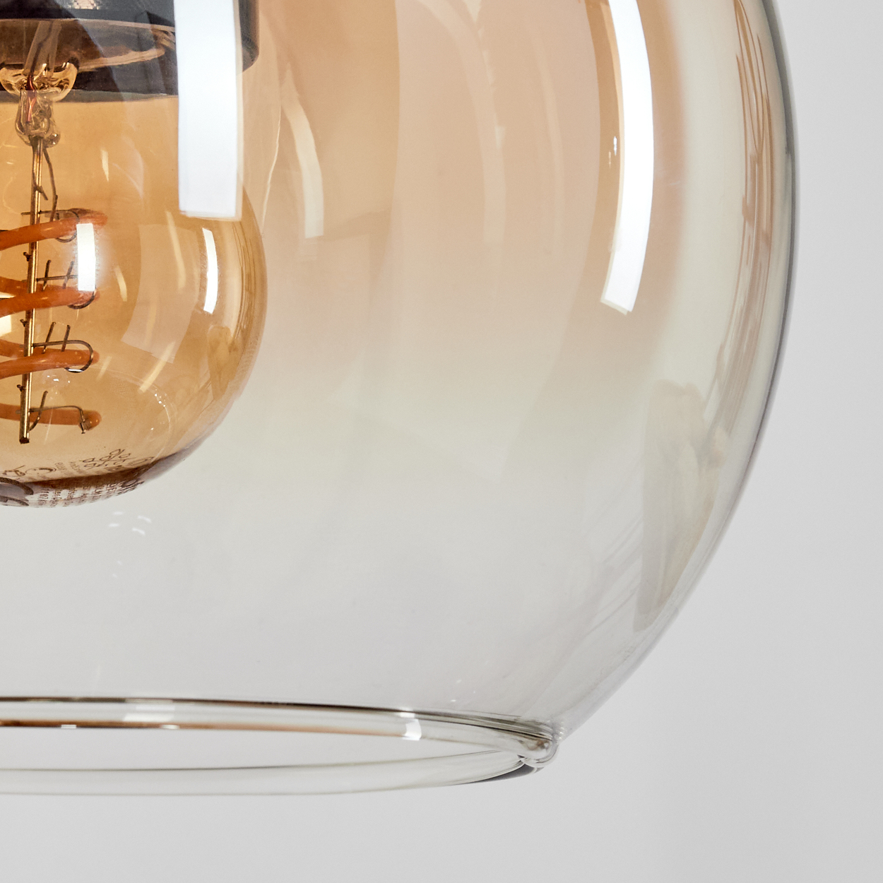 Nahaufnahme einer Glasleuchte. Ein klarer Glasschirm umgibt eine Glühbirne mit orangem Glühfaden, vor weißem Hintergrund.