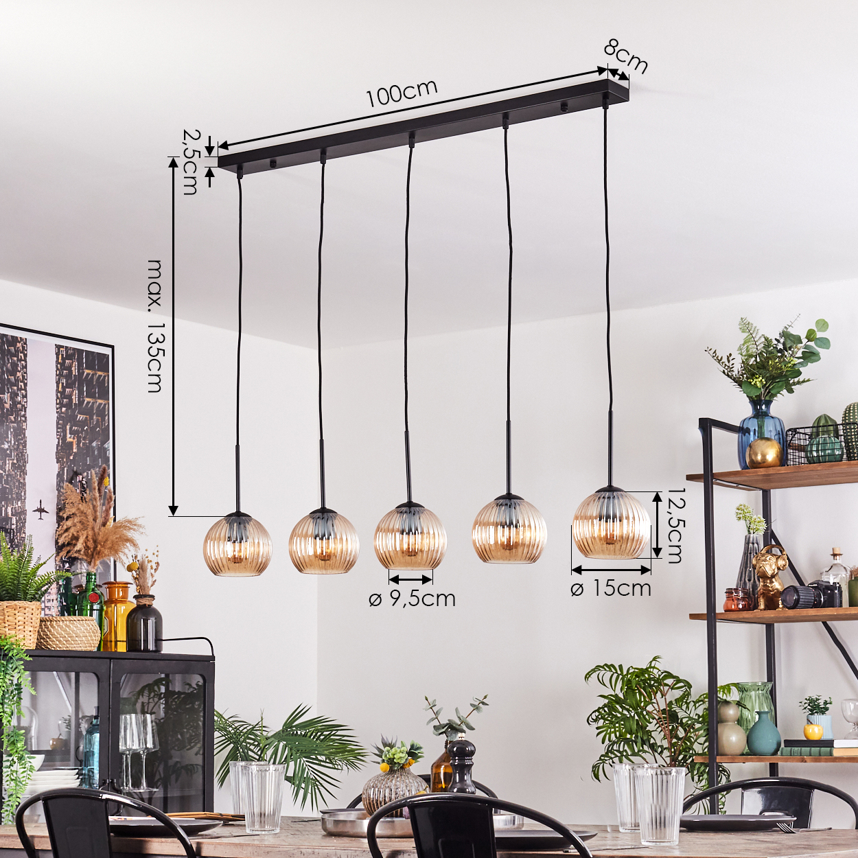 Fünf-Licht-Pendelleuchte mit bernsteinfarbenen Glasschirmen über einem Esstisch. Maße sind angegeben. Hintergrund enthält Regale und Pflanzen.