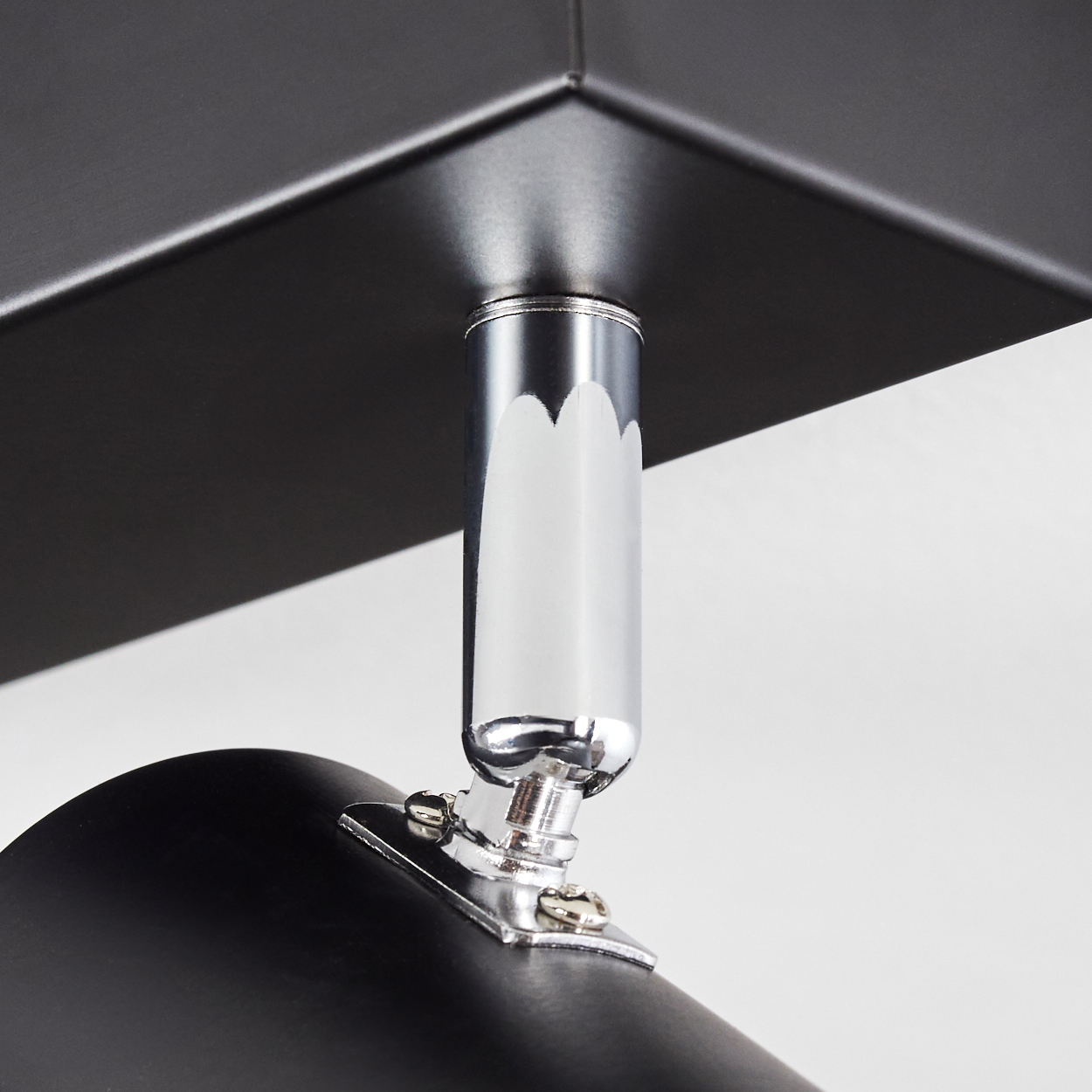 Nahaufnahme einer modernen schwarzen Lampe. Sie hat ein Chromgelenk und ist an einer dunklen quadratischen Oberfläche befestigt. Weißer Hintergrund.