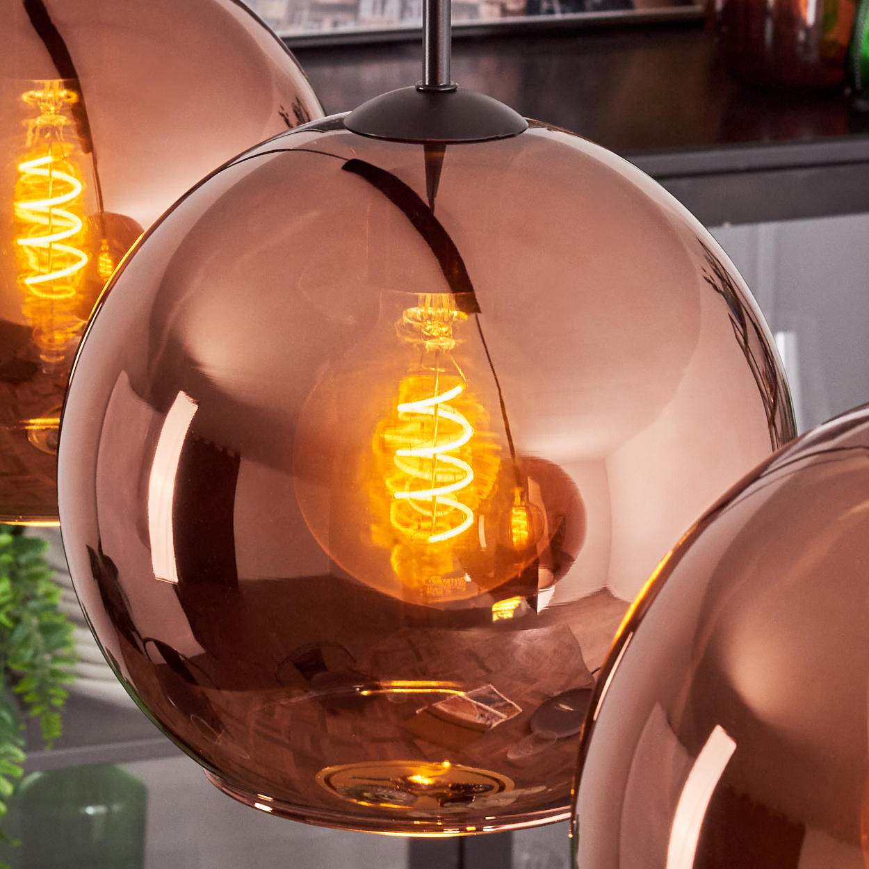 Drei kupferfarbene Kugelleuchten mit leuchtenden Spiralbirnen. Die Glühbirnen strahlen ein warmes orangefarbenes Licht aus.