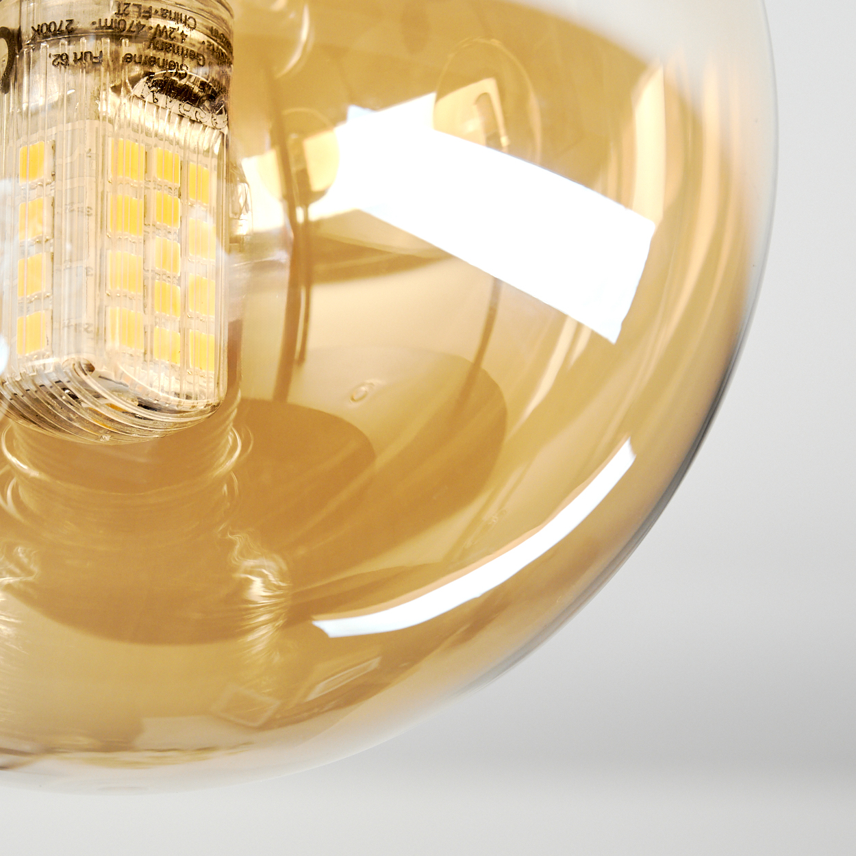 Nahaufnahme einer Glühbirne. Die Birne ist aus Glas und hat einen gelben Farbton. Die Lichtquelle ist sichtbar.