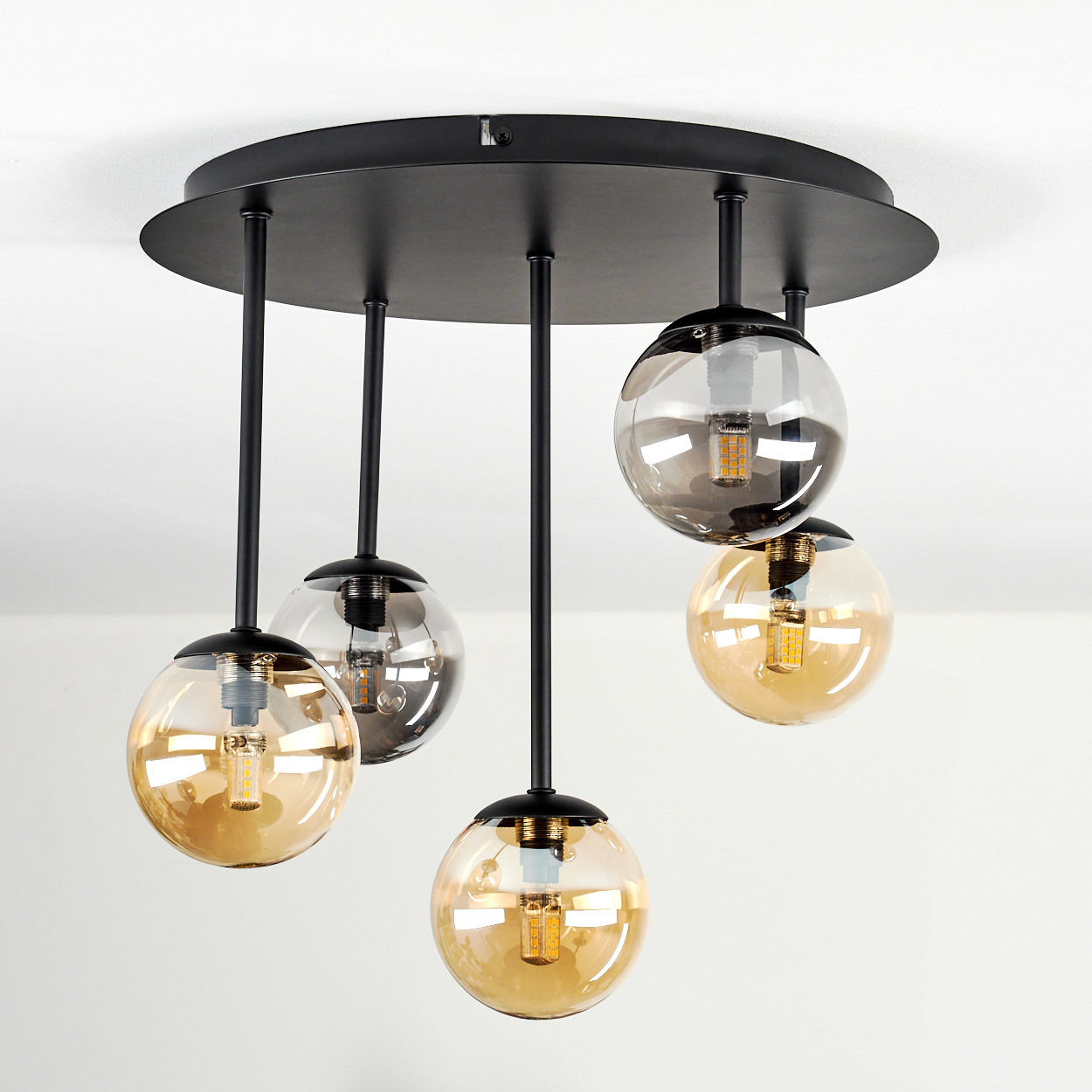 Eine moderne Deckenleuchte mit fünf Glaskugel-Schirmen und schwarzen Stangen. Die Schirme haben bernsteinfarbene und graue Farbtöne und LEDs.