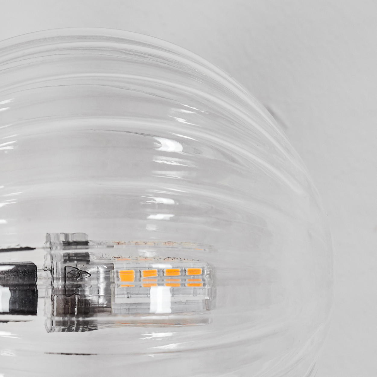 Nahaufnahme einer klaren Glühbirne, die die internen orangen LED-Leuchten und den Metallsockel vor weißem Hintergrund zeigt.