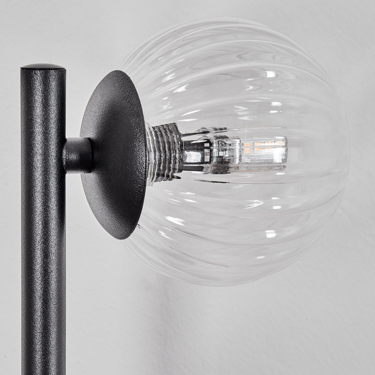 Eine moderne Lampe mit schwarzem Metallsockel und einer transparenten, gerippten Glaskugel. Die Glühbirne ist im Inneren sichtbar.