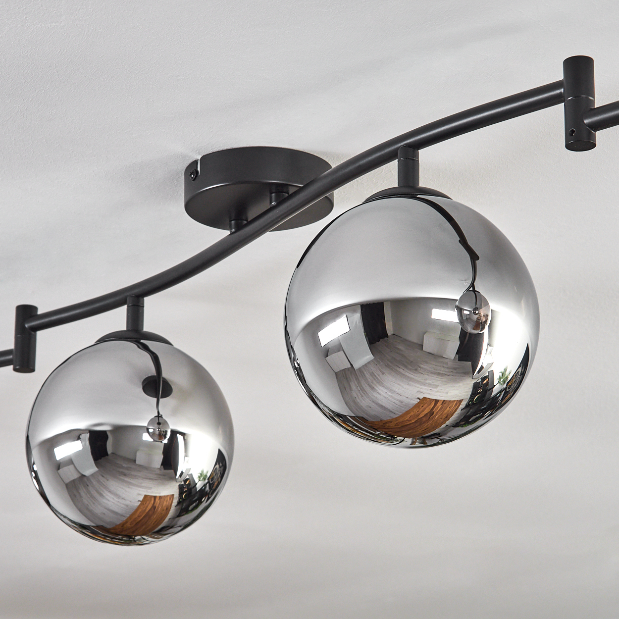 Nahaufnahme einer modernen Deckenleuchte. Sie hat drei reflektierende Chromkugel-Lichter und ein schwarzes Metallgestell an einer weißen Decke.