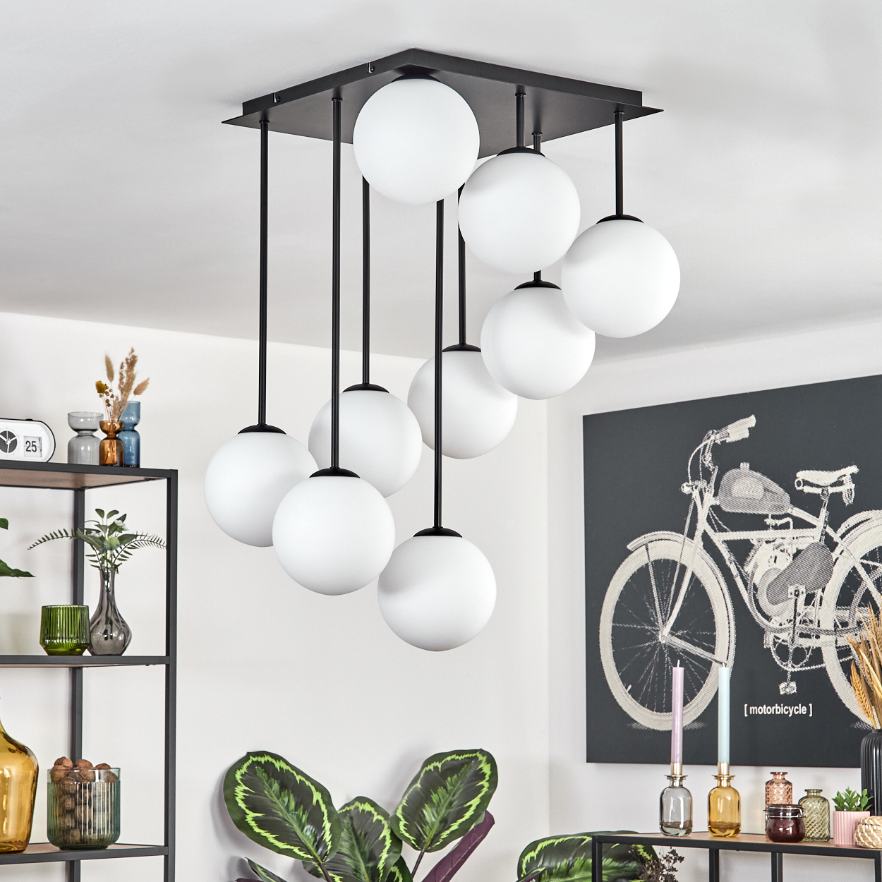 Eine moderne Deckenlampe mit weißen Kugeln. Eine schwarze quadratische Basis hält die Lichter. Kunstwerk eines Fahrrads, Kerzen und Pflanzen sind ebenfalls vorhanden.