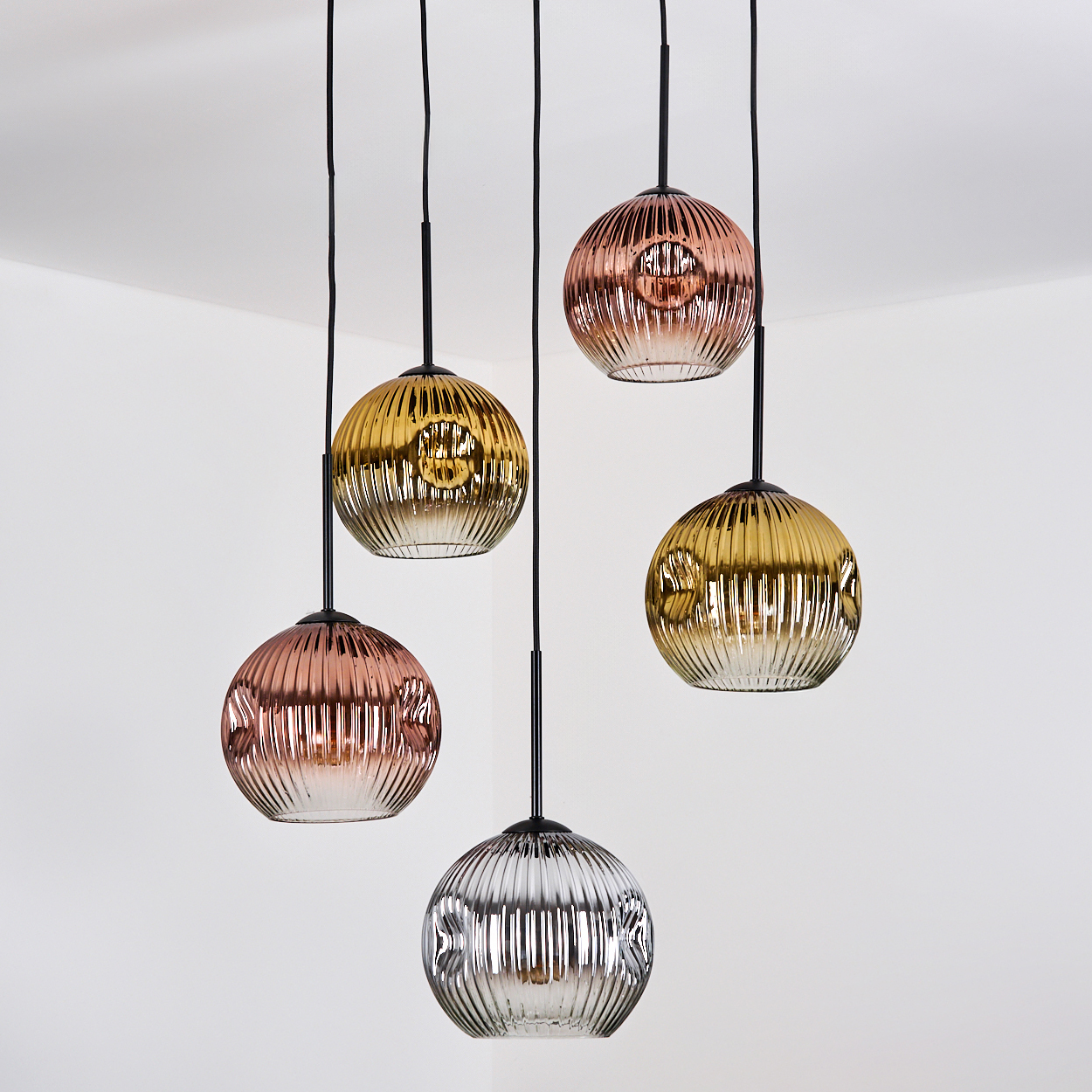 Fünf hängende Kugelpendant-Leuchten in verschiedenen Farben: Gold, Kupfer und Silber, vor einem weißen Eckhintergrund.