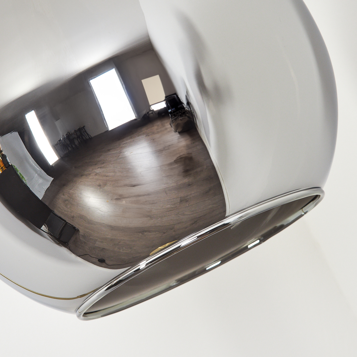 Ein reflektierendes, kugelförmiges Objekt, das die Reflexion eines Raumes zeigt. Der Raum hat Holzböden, Fenster und Studioausrüstung.