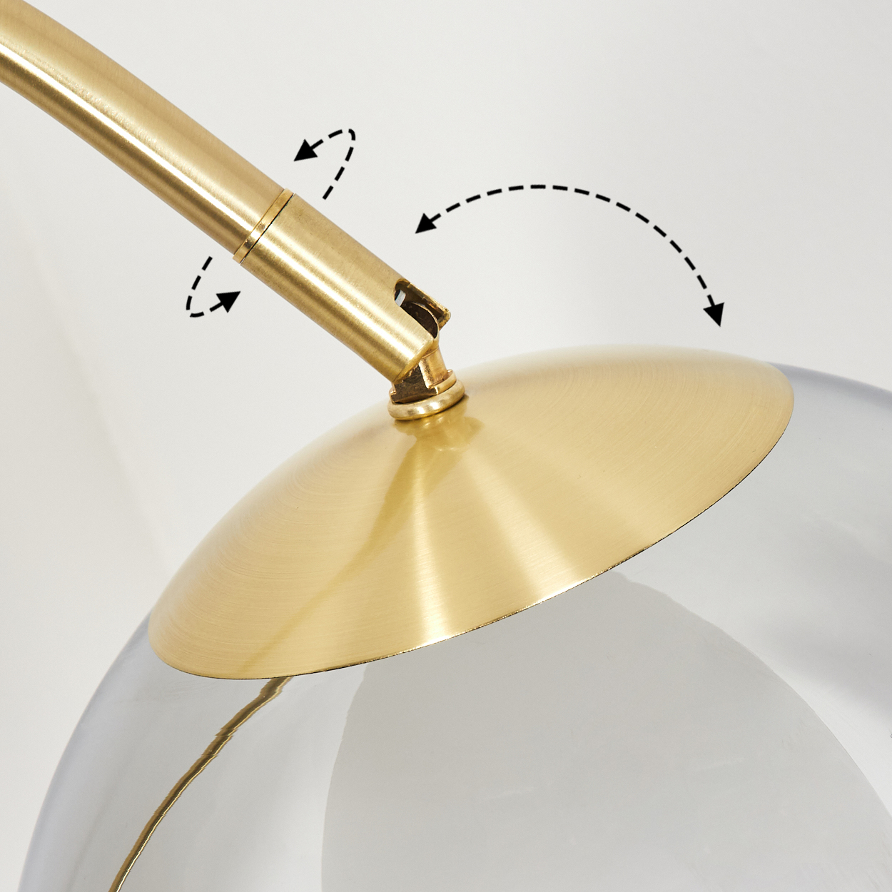 Nahaufnahme einer Messinglampe. Sie hat einen gebogenen Arm, einen goldenen Sockel und einen transparenten Glasschirm. Pfeile zeigen die Bewegung.