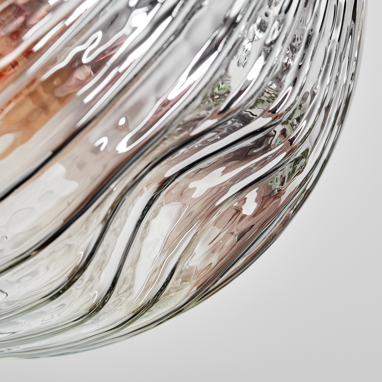 Nahaufnahme eines Glasobjekts mit Wellenmuster. Das Glas reflektiert Licht und Farben, vor weißem Hintergrund.