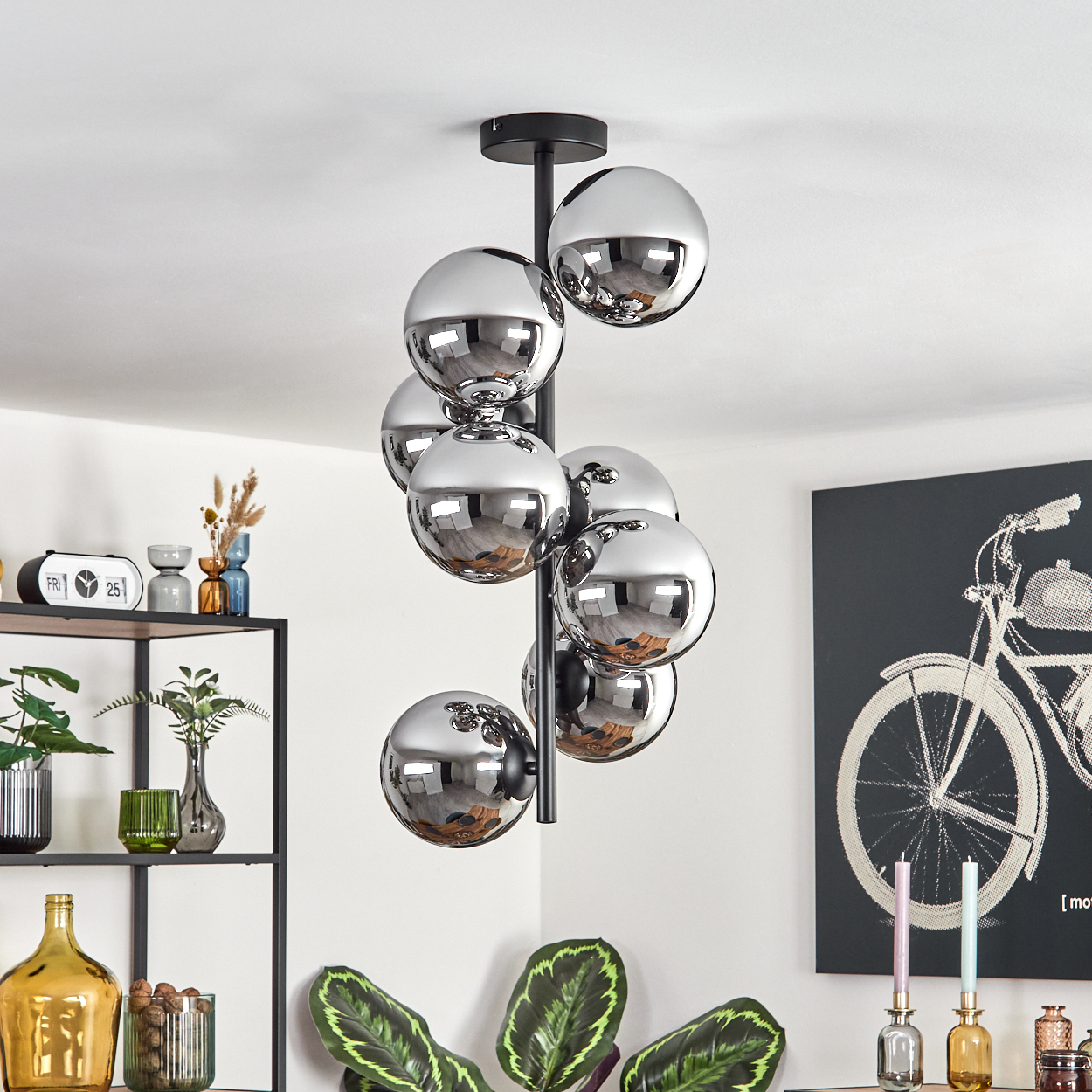 Eine moderne Deckenleuchte mit Chromkugeln hängt von der Decke. Ein schwarzes Regal mit Dekor und ein Fahrradkunstwerk sind sichtbar.