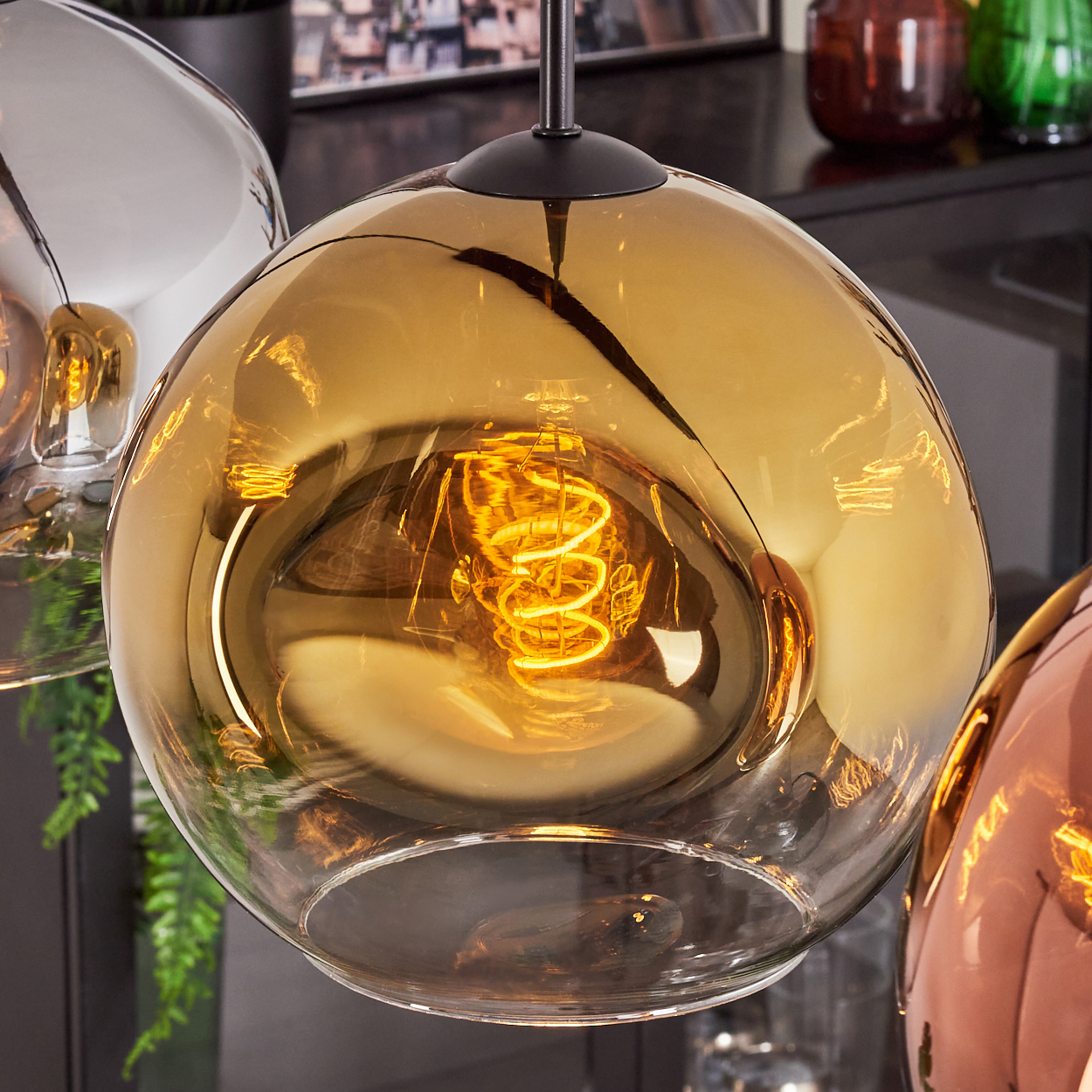 Nahaufnahme einer Glaskugel-Leuchte. Im Inneren leuchtet eine Spiralfaser. Andere ähnliche Leuchten sind teilweise sichtbar.