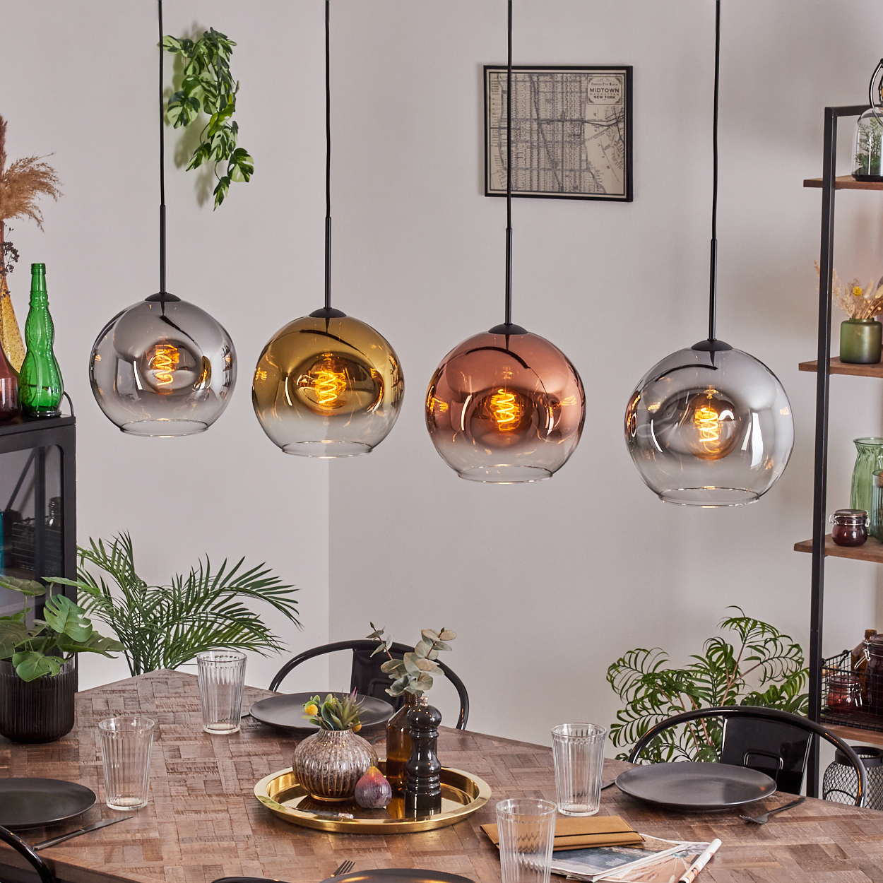 Esszimmer mit Holztisch, vier Pendelleuchten, Gläsern, Pflanzen und einer Karte an der Wand. Die Lampen haben verschiedene Farben.