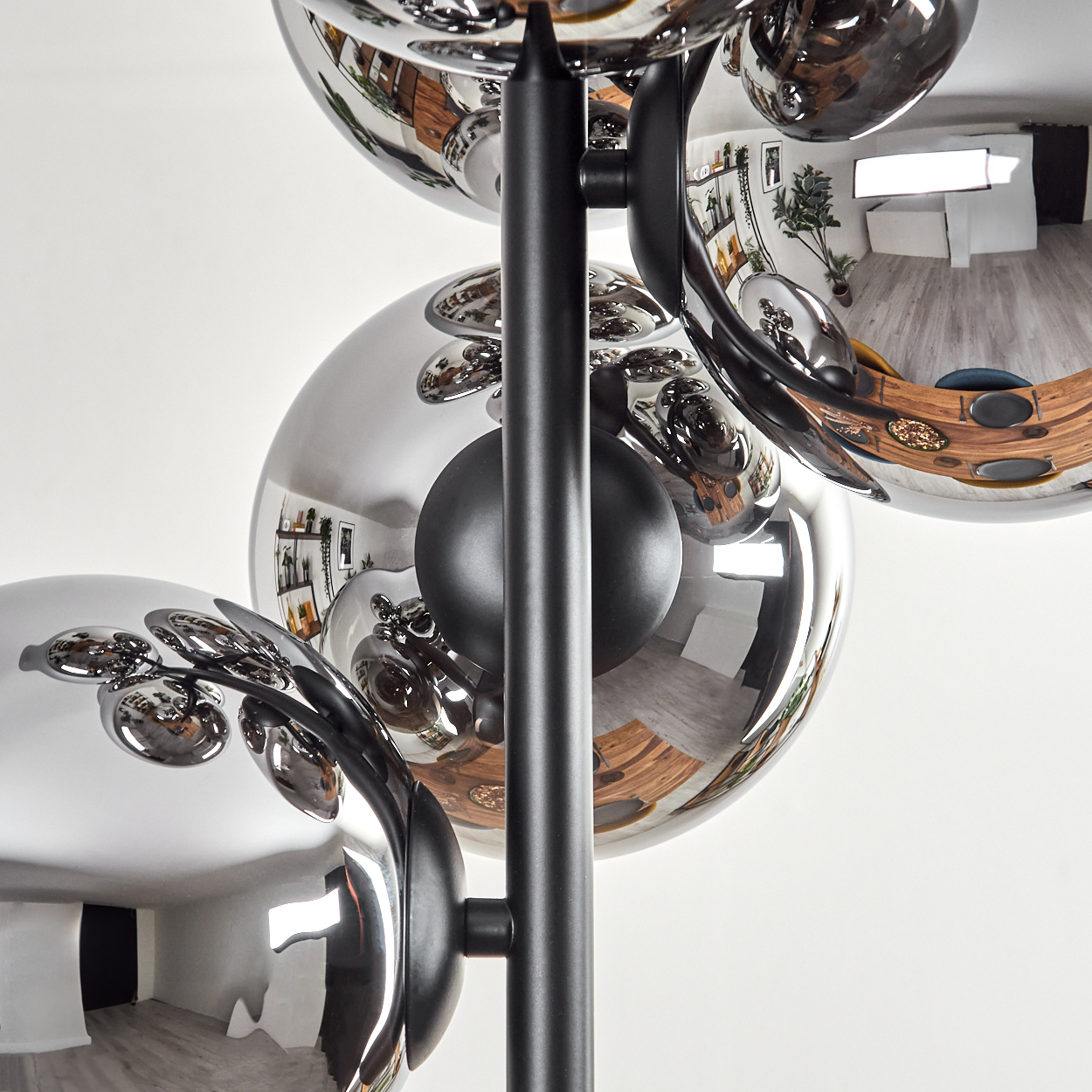 Eine moderne Lampe mit Chromkugeln, die einen Raum mit Holztisch, Pflanzen und weißen Wänden reflektieren.