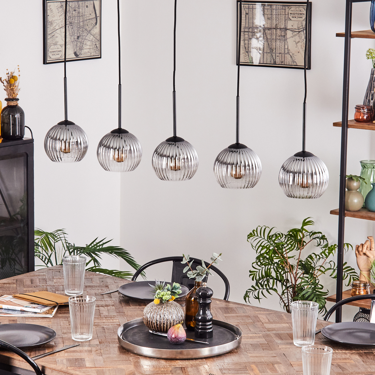 Esszimmer: Fünf Pendelleuchten über einem Holztisch, der für ein Essen gedeckt ist. Pflanzen und Regale im Hintergrund.