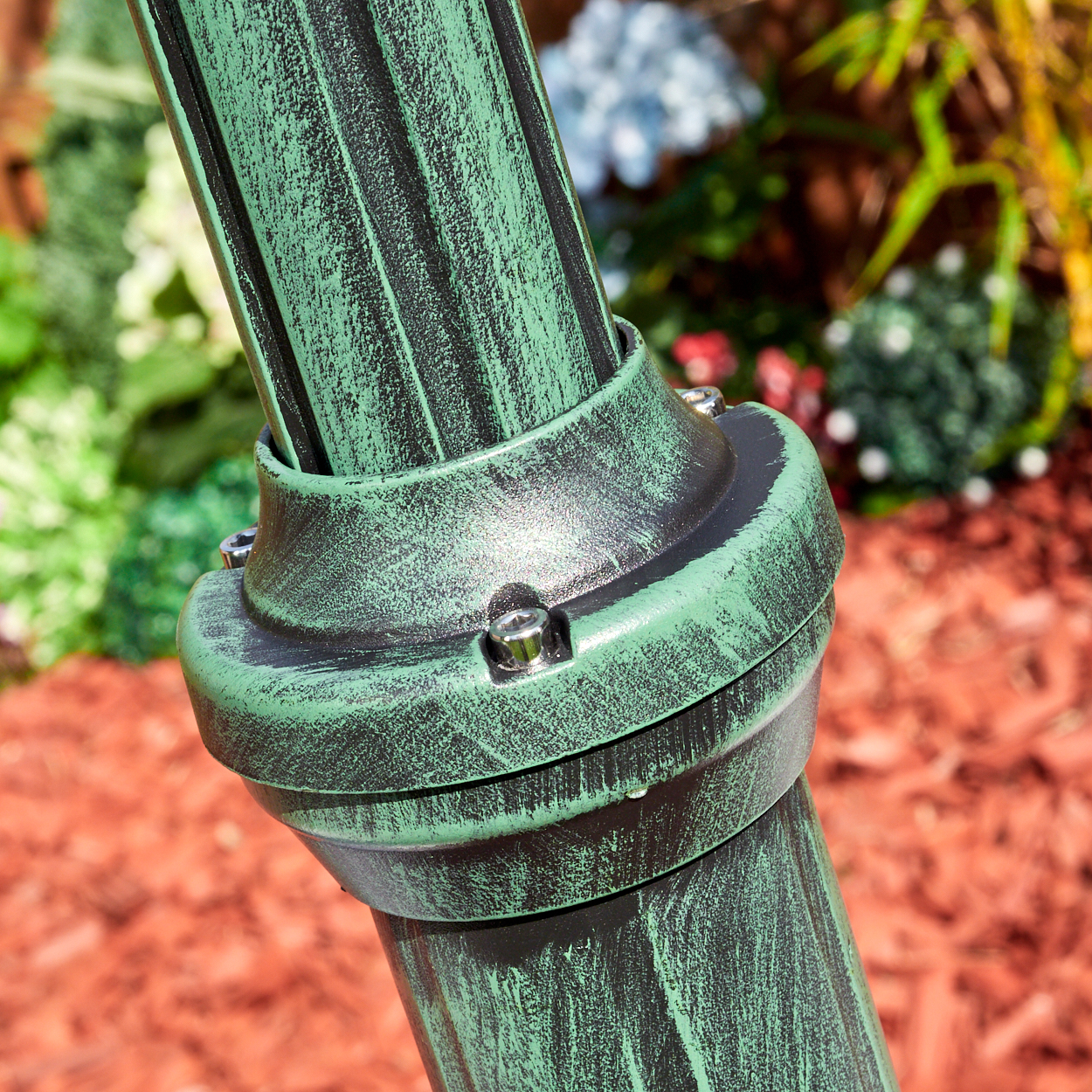 Nahaufnahme eines grün-schwarzen Metallstabs mit Verbindungsring, vor verschwommenem Gartenhintergrund.