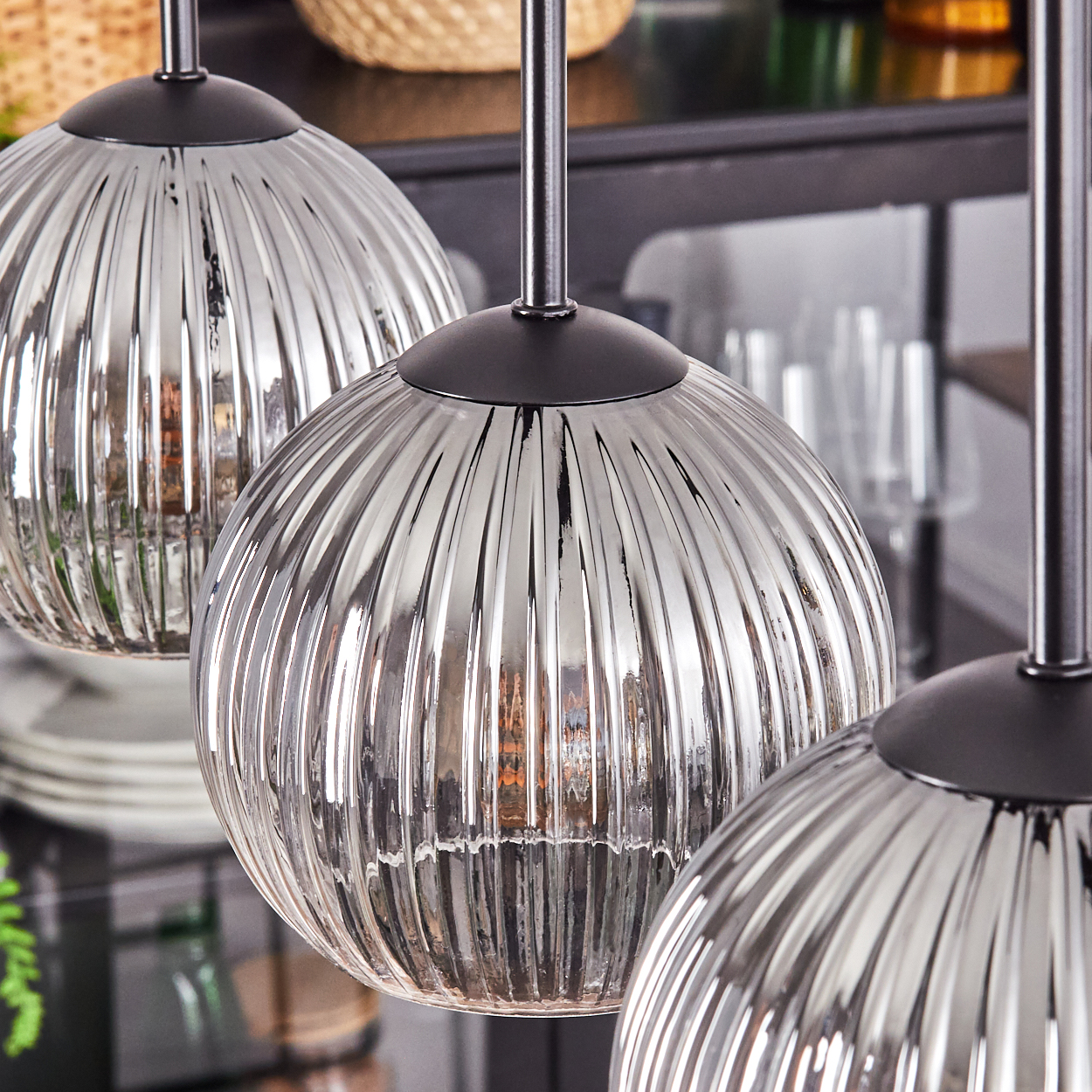 Drei silberne, geriffelte Glas-Pendelleuchten hängen von der Decke. Im unscharfen Hintergrund ist ein Kücheninterieur zu sehen.