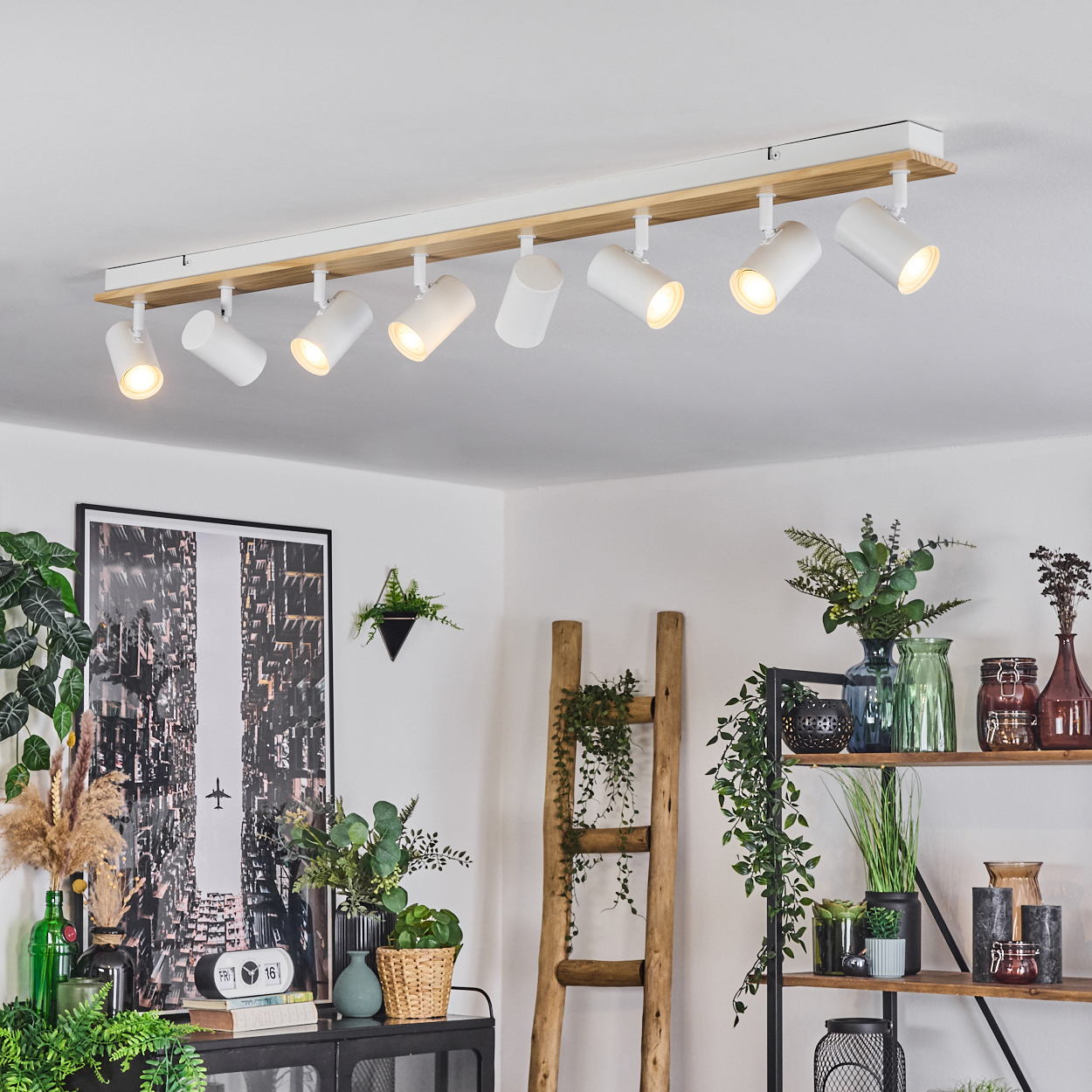 Ein moderner Raum mit einer Deckenleuchte. Pflanzen, Kunst und Regale mit Dekorationen befinden sich im Raum.