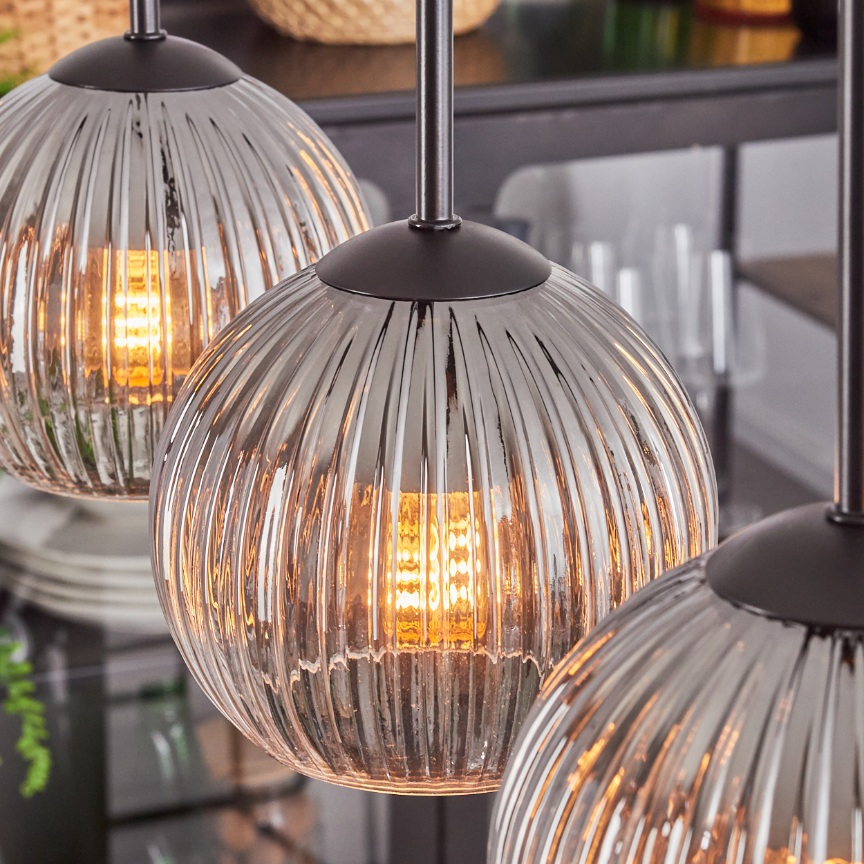 Drei Pendelleuchten aus Glas mit warmen Innenlichtern. Gerippte Glasschirme hängen an schwarzen Metallstangen.