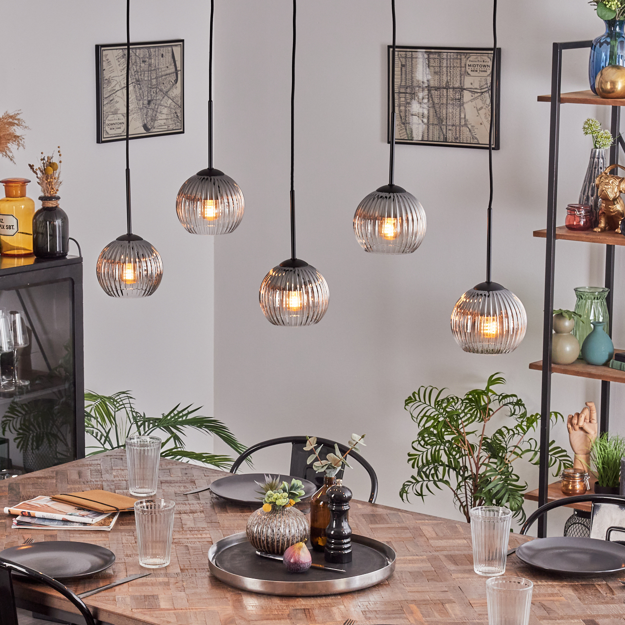 Esszimmer mit Holztisch, Hängelampen, Tellern, Gläsern und einem dekorativen Tablett in der Mitte.
