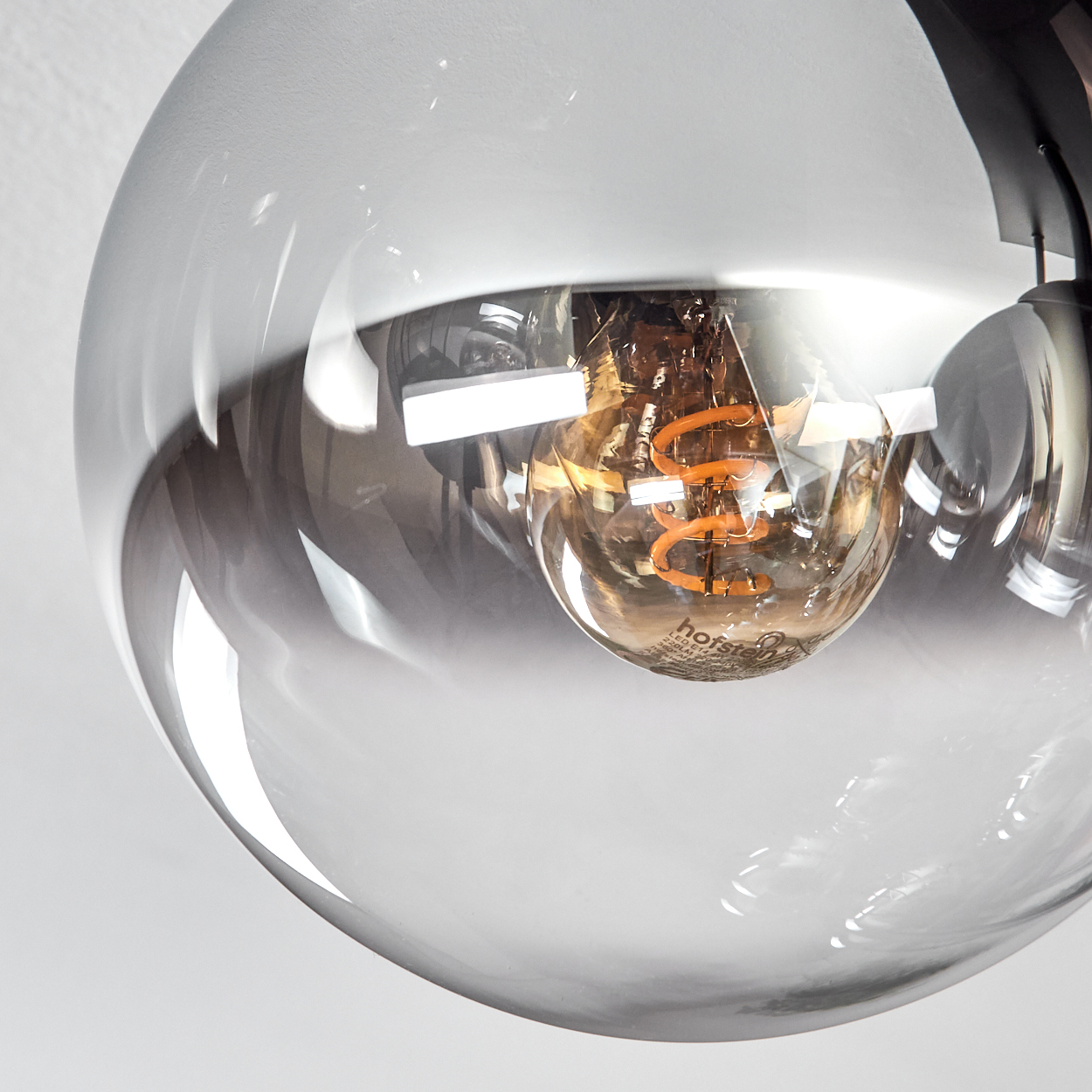 Nahaufnahme einer Glaskugel-Leuchte. Im Inneren eine Glühbirne mit einer orangefarbenen Spule. Die Kugel reflektiert die Umgebung.