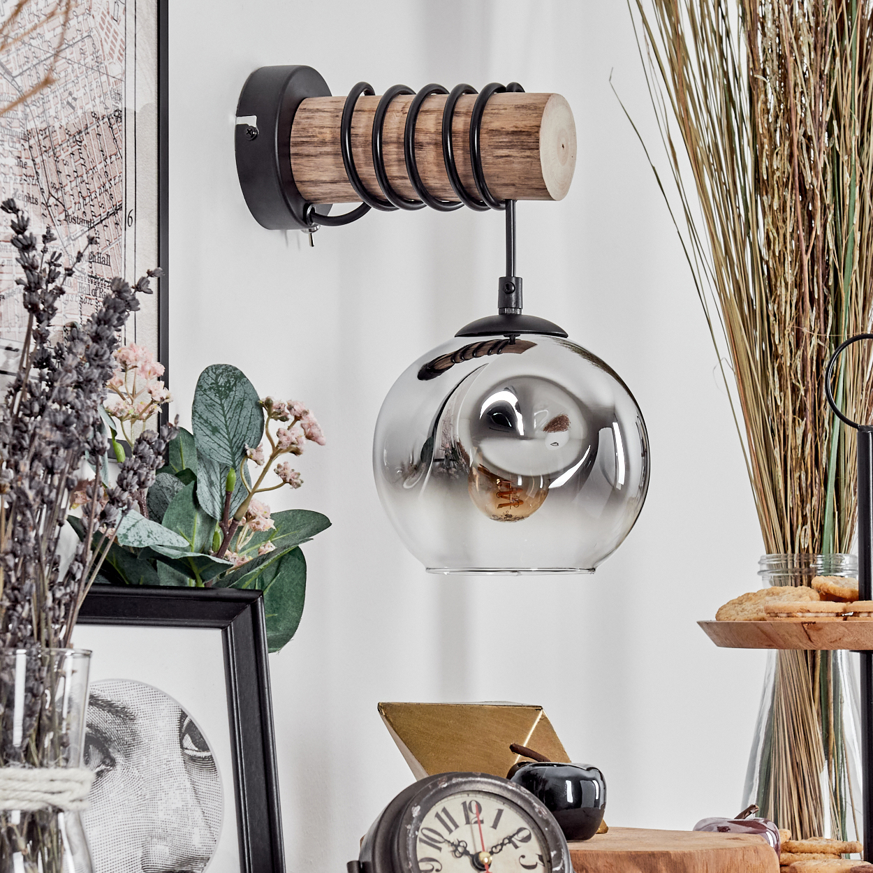 Eine dekorative Wandlampe mit Glasschirm und Holzelementen. Weitere Dekorationen sind Blumen, eine Uhr und Kekse.