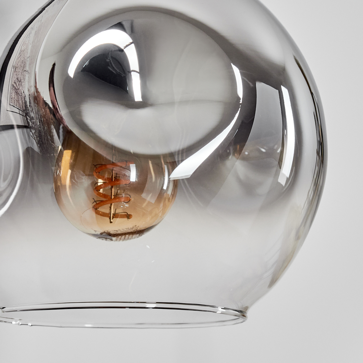 Nahaufnahme einer Glasleuchte mit einer Glühbirne im Inneren. Das Glas ist klar und reflektierend. Der Hintergrund ist weiß.