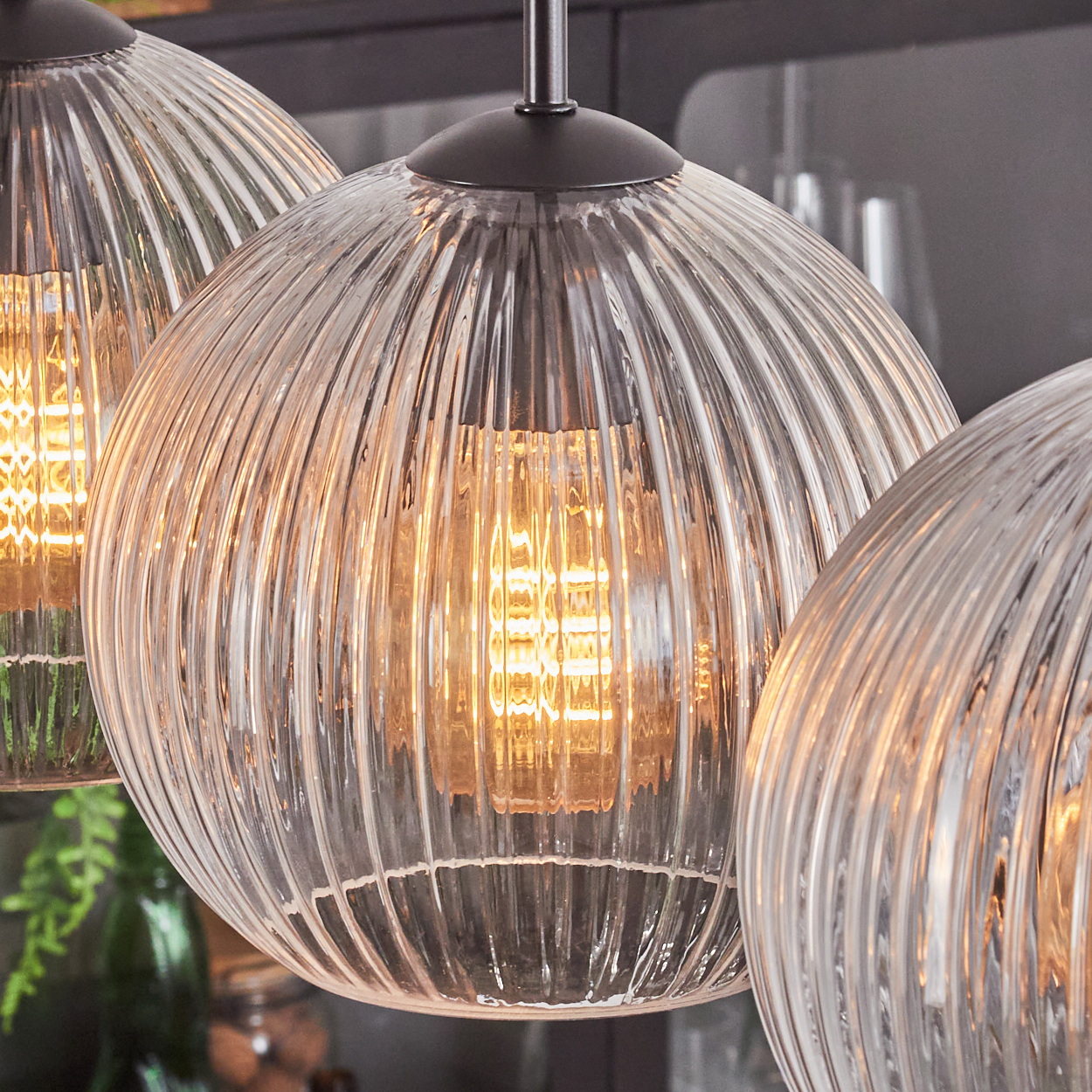 Nahaufnahme von drei Glas-Pendelleuchten mit geripptem Design. Jede hat eine warme Glühbirne im Inneren, die an einer dunklen Halterung hängt.