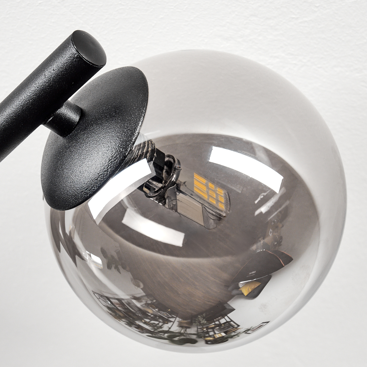 Nahaufnahme einer modernen Lampe. Sie hat einen schwarzen Arm, einen runden schwarzen Schirm und eine transparente Glaskugel. Die Glühbirne ist sichtbar.