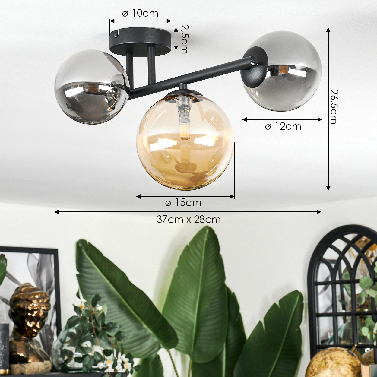 Moderne Deckenlampe mit drei Glaskugeln, Maße beschriftet. Grüne Pflanzen im Vordergrund, Deko und Wand im Hintergrund.