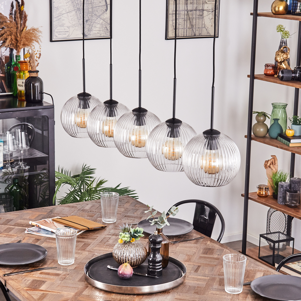 Esszimmer mit Holztisch, Hängelampen und Regal mit Dekorationen. Tisch für eine Mahlzeit gedeckt.