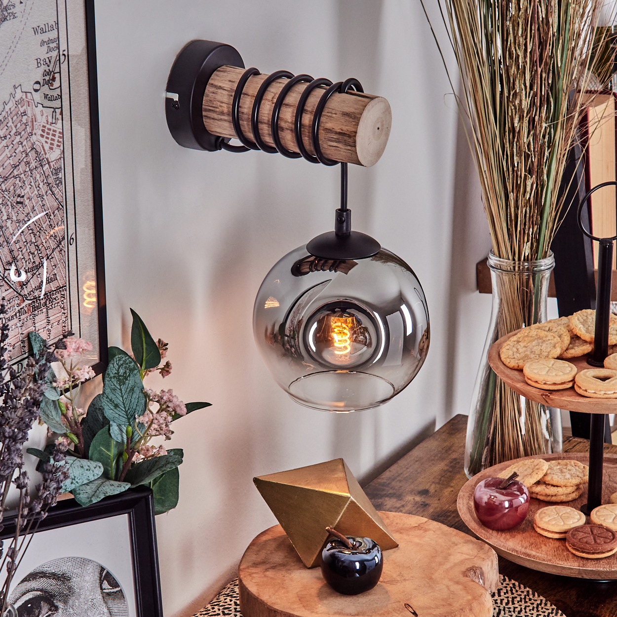 Eine dekorative Wandlampe mit Glasschirm, Holzakzenten und einer freiliegenden Glühbirne. Weitere Dekorationen sind Kekse und eine Karte.