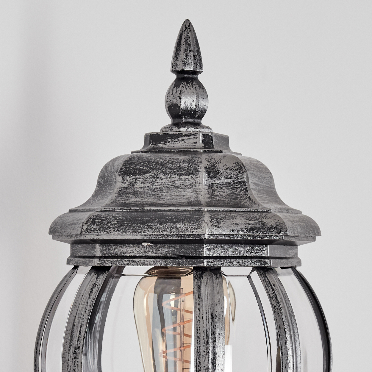 Nahaufnahme einer dekorativen Lampe. Sie hat eine silberne Oberfläche, klares Glas und eine freiliegende Glühbirne. Der Hintergrund ist weiß.