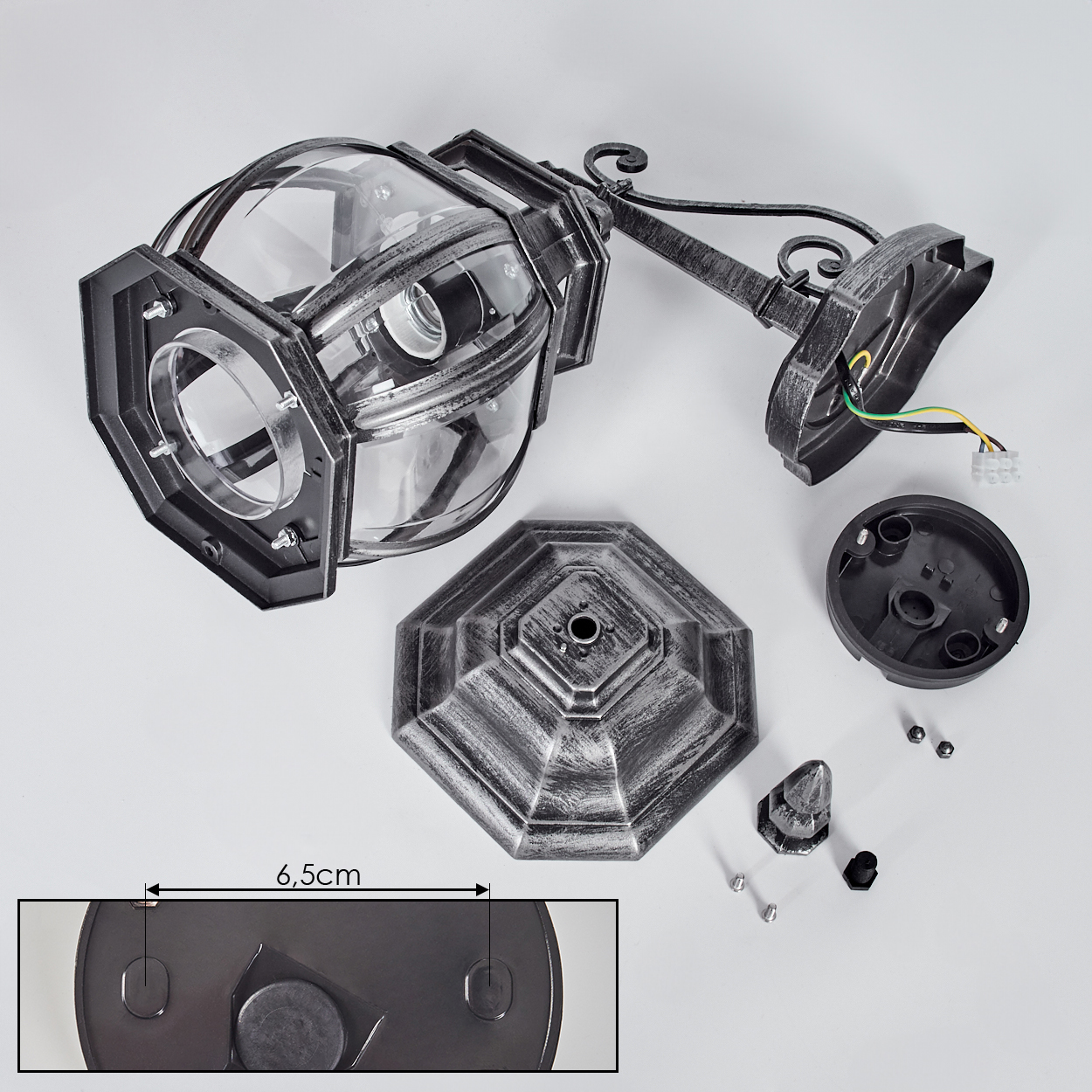 Zerlegte Außenlampe auf Weiß. Teile umfassen Lampenkopf, Sockel, Montagearm und kleine Komponenten, alle in Grau und Schwarz.