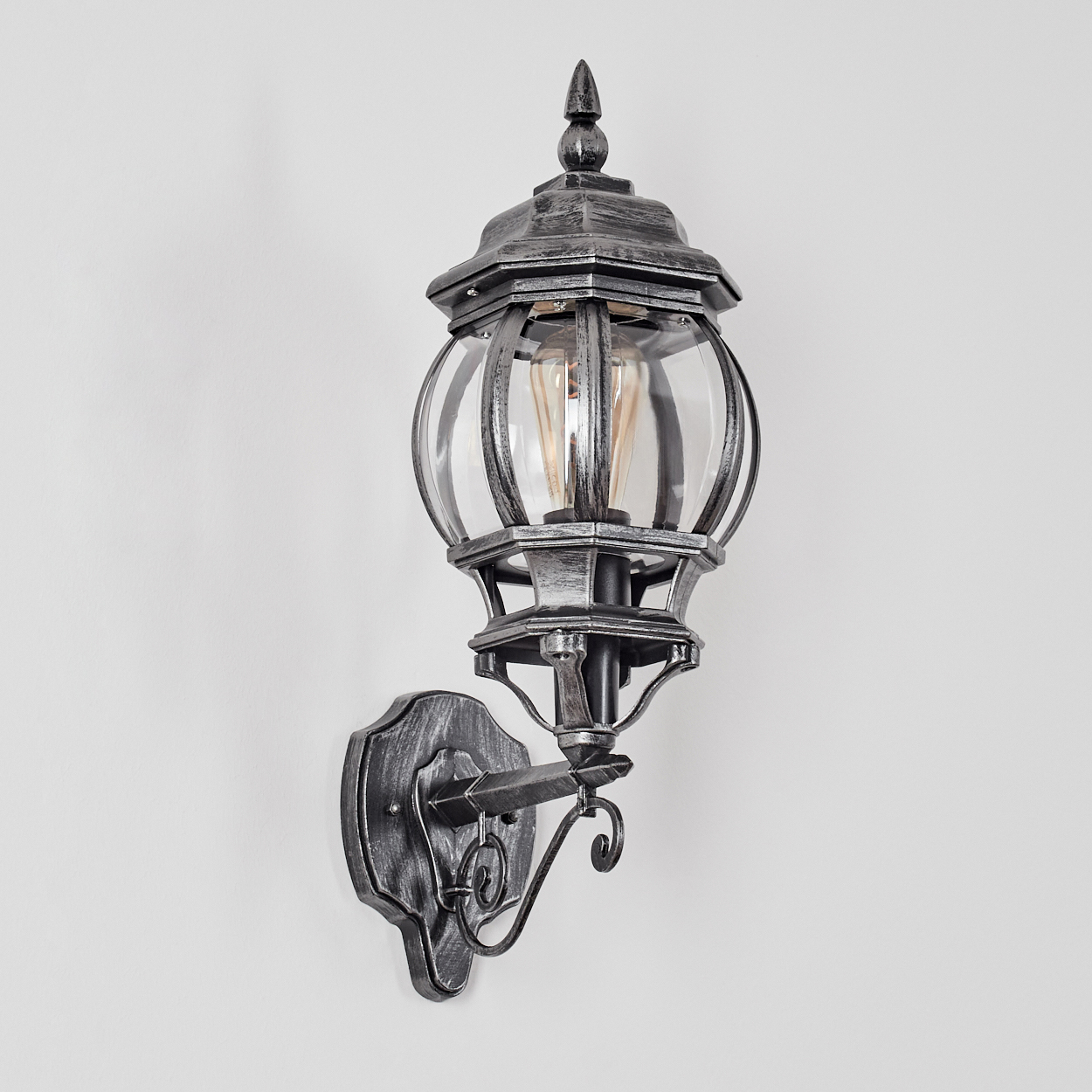 Eine verzierte, grau Wandleuchte mit Glaskugel. Sie ist an einer weißen Wand befestigt. Die Lampe hat ein dekoratives Design.