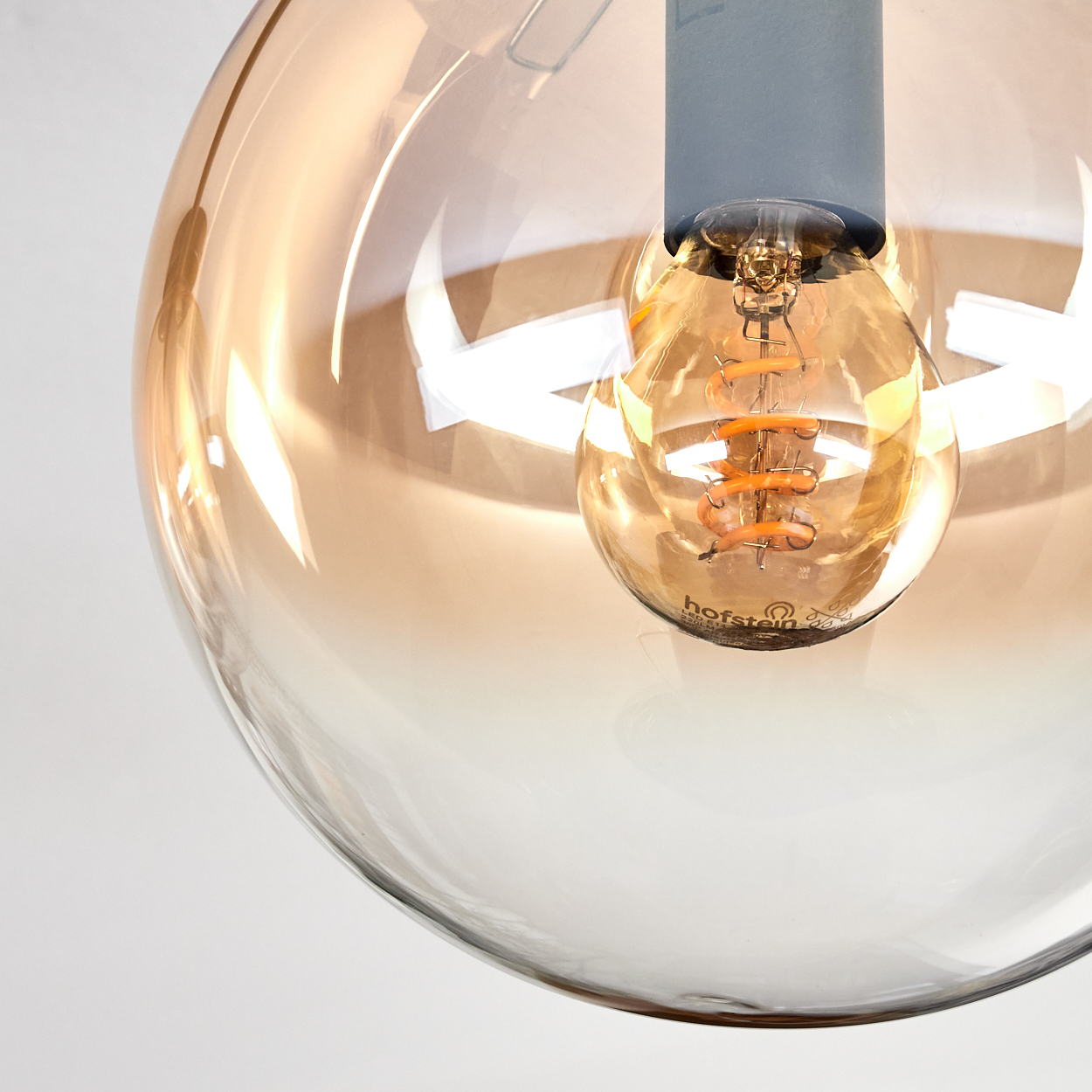 Nahaufnahme einer Glühbirne in einer Glaskugel. Die Glühbirne leuchtet. Das Glas hat einen Farbverlauf von Braun und Klar.