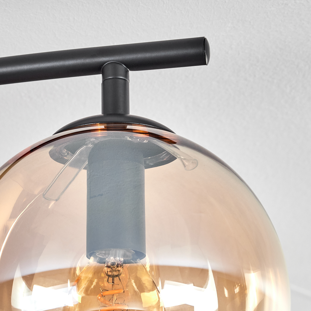 Nahaufnahme einer modernen Leuchte. Sie hat einen schwarzen Metallrahmen und einen bernsteinfarbenen Glasschirm. Im Inneren befindet sich eine Glühbirne.