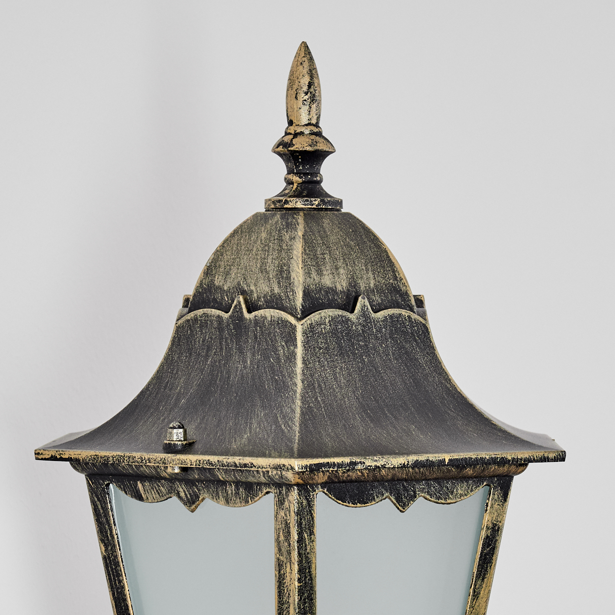 Nahaufnahme einer dekorativen Außenlampe mit schwarzem und goldenem Finish. Sie hat eine spitze Spitze und Milchglasscheiben.