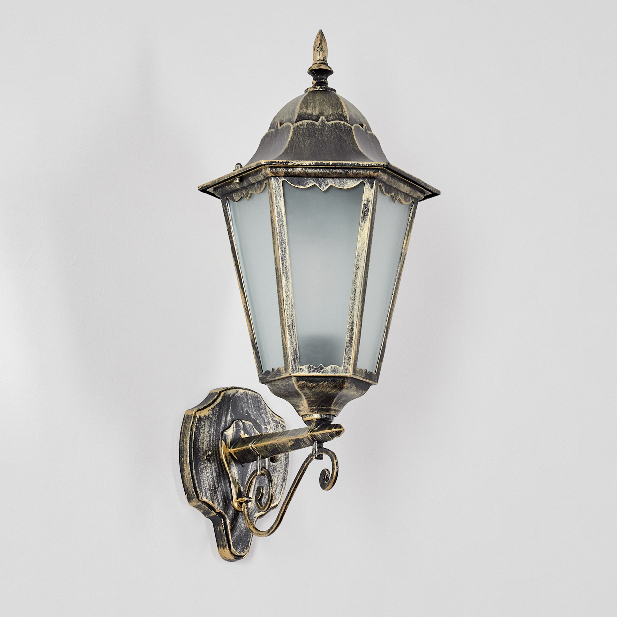 Eine verzierte Wandlampe mit Milchglasscheiben, Gold- und Schwarz-Finish, an einer weißen Wand montiert. Dekoratives Design mit Schnörkeln.