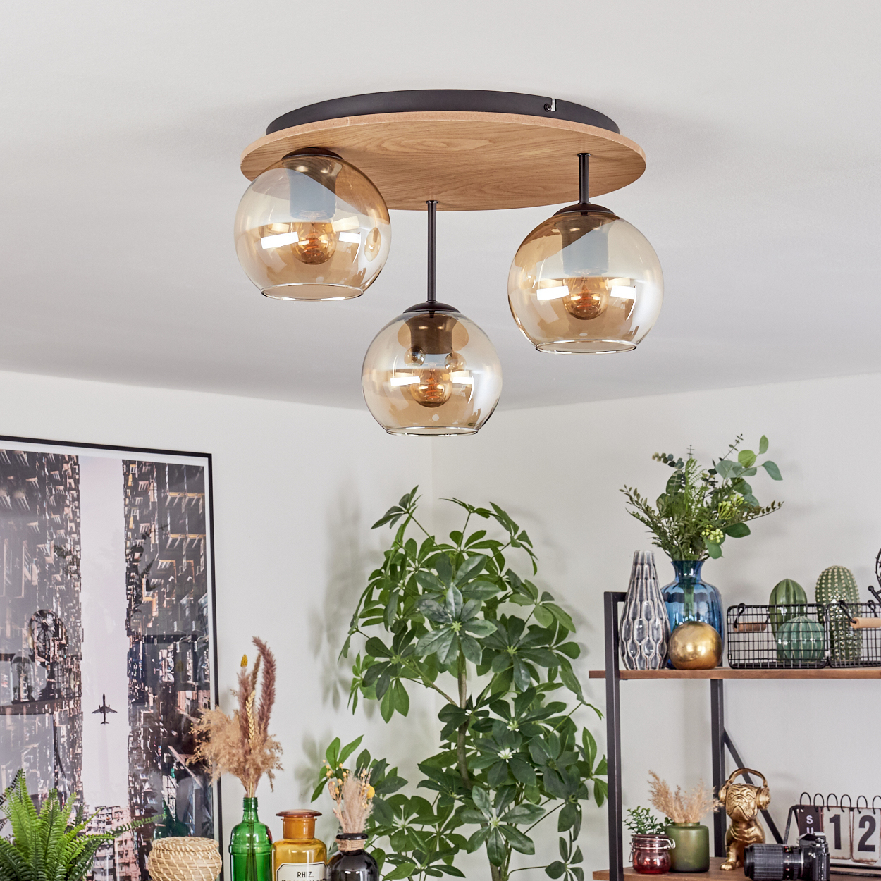 Moderne Deckenlampe mit drei kugelförmigen Schirmen. Darunter Pflanzen und Dekorationsartikel auf einem Regal und Wandkunst.
