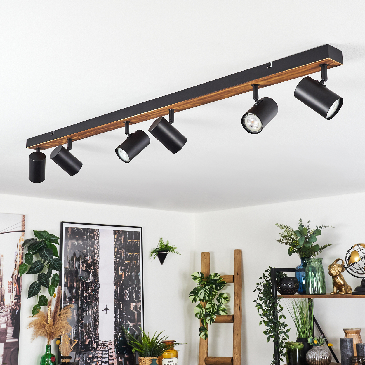 Schwarze Strahler an einem Holzbalken an der Decke, die einen Raum mit Dekoration, Pflanzen und Kunst beleuchten.