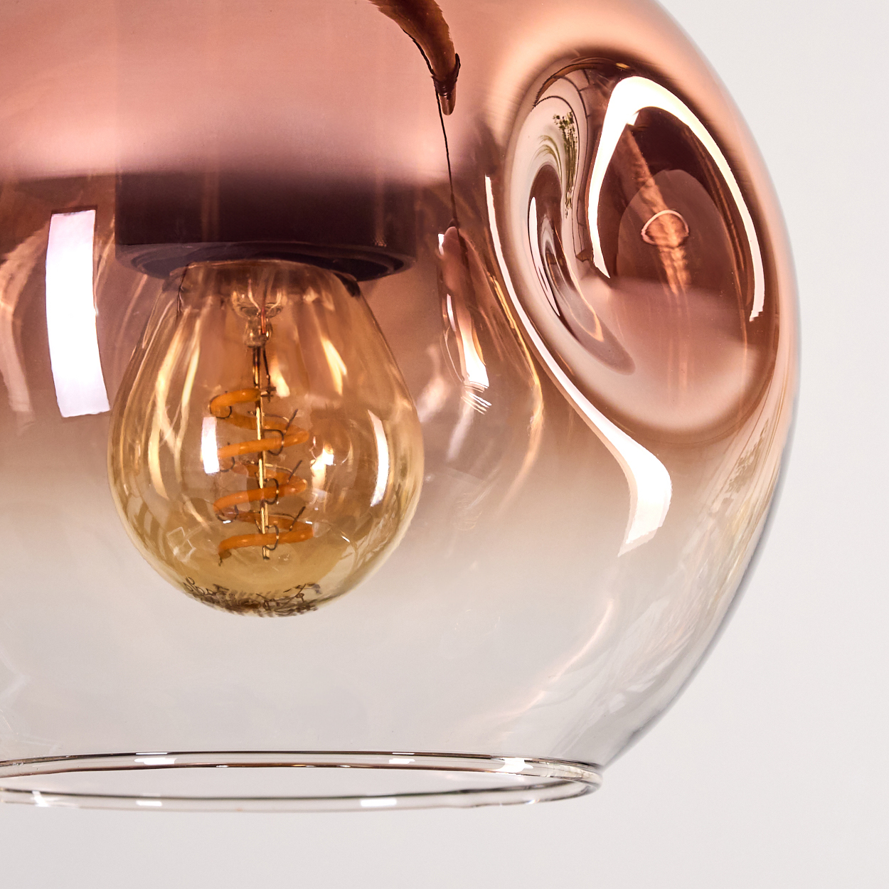 Nahaufnahme einer Glas-Pendelleuchte. Die Leuchte hat einen kupferfarbenen Schirm mit einer sichtbaren Glühbirne.
