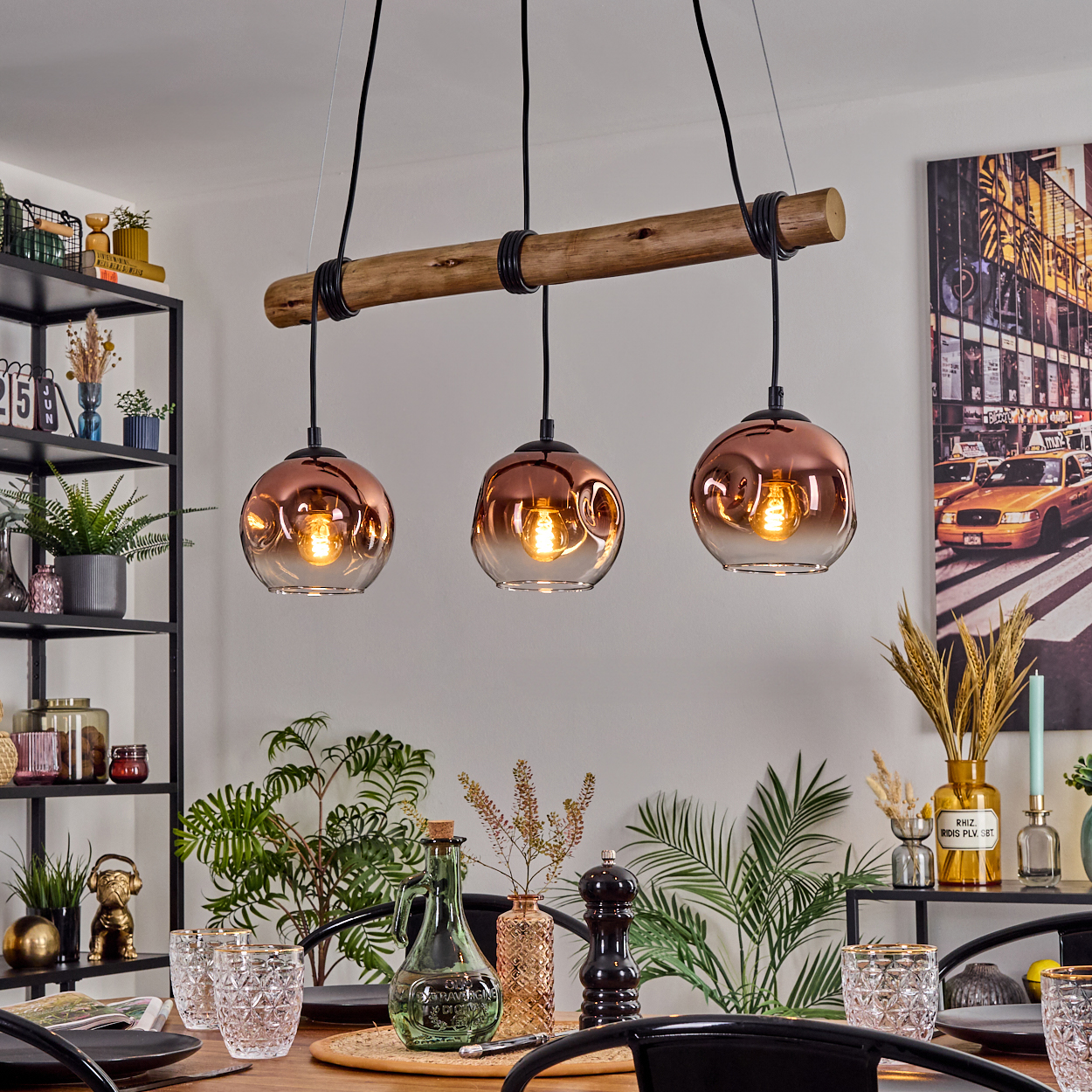 Esszimmer mit kupferfarbenen Pendelleuchten über einem Holztisch, Pflanzen und Kunst. Regale mit Dekoration sind sichtbar.