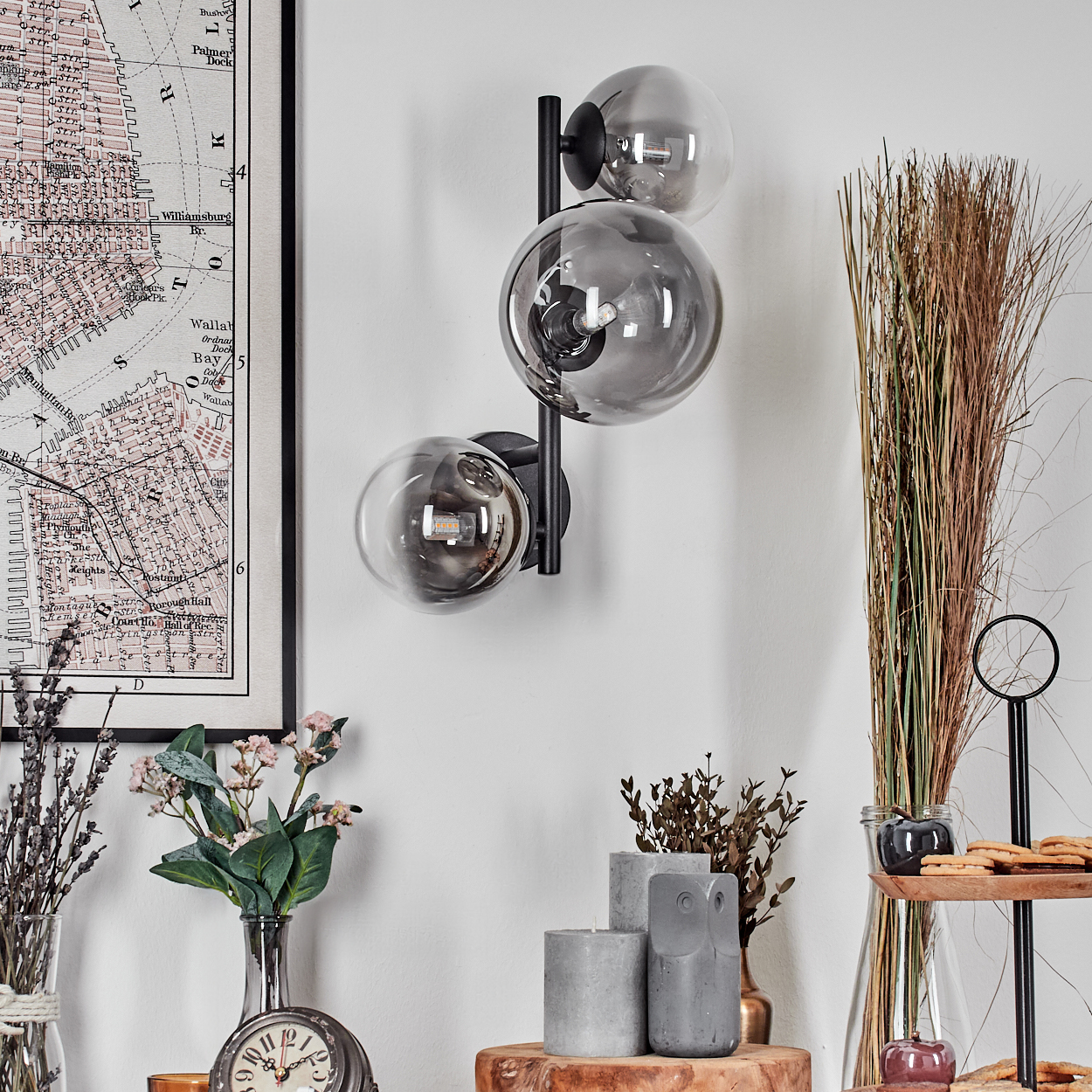 Ein modernes Interieur mit Wandlampe, Blumen, Kerzen und einer Karte. Die Lampe hat drei Glaskugeln. Verschiedene dekorative Gegenstände sind ausgestellt.