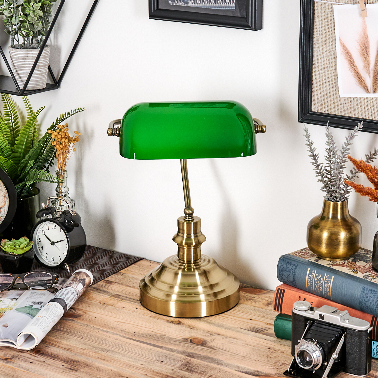 Eine grüne Bankerlampe steht auf einem Holztisch. Bücher, Kamera und Dekorationen umgeben sie.