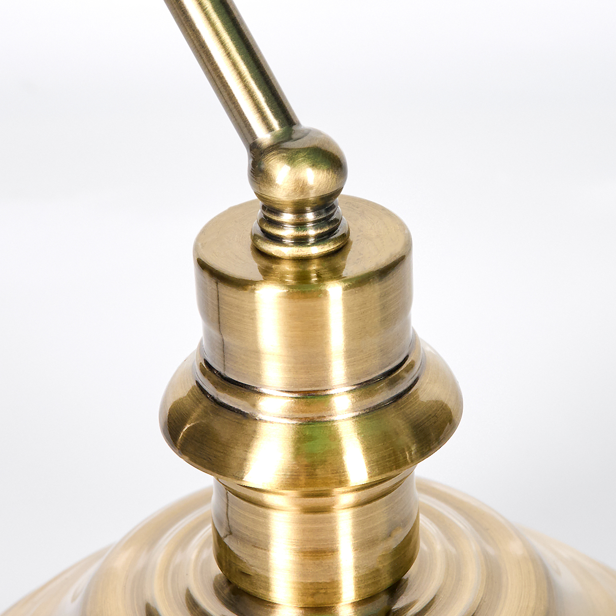 Nahaufnahme einer Messinglampenhalterung. Die Lampe hat einen gebogenen Arm und einen detaillierten Sockel. Der Hintergrund ist weiß.
