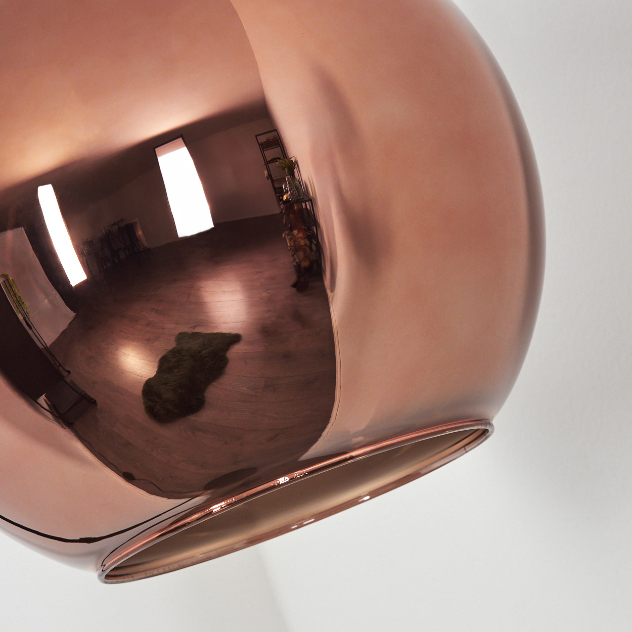 Eine kupferfarbene, kugelförmige Lampe spiegelt einen Raum mit Holzböden, einem grünen Teppich und einem Regal wider. Der Hintergrund ist weiß.