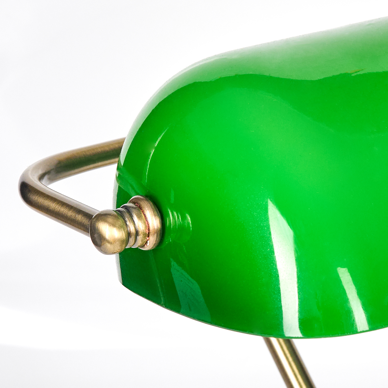Nahaufnahme einer grünen Schreibtischlampe. Der Lampenschirm ist grün, der Sockel und der Griff messingfarben.