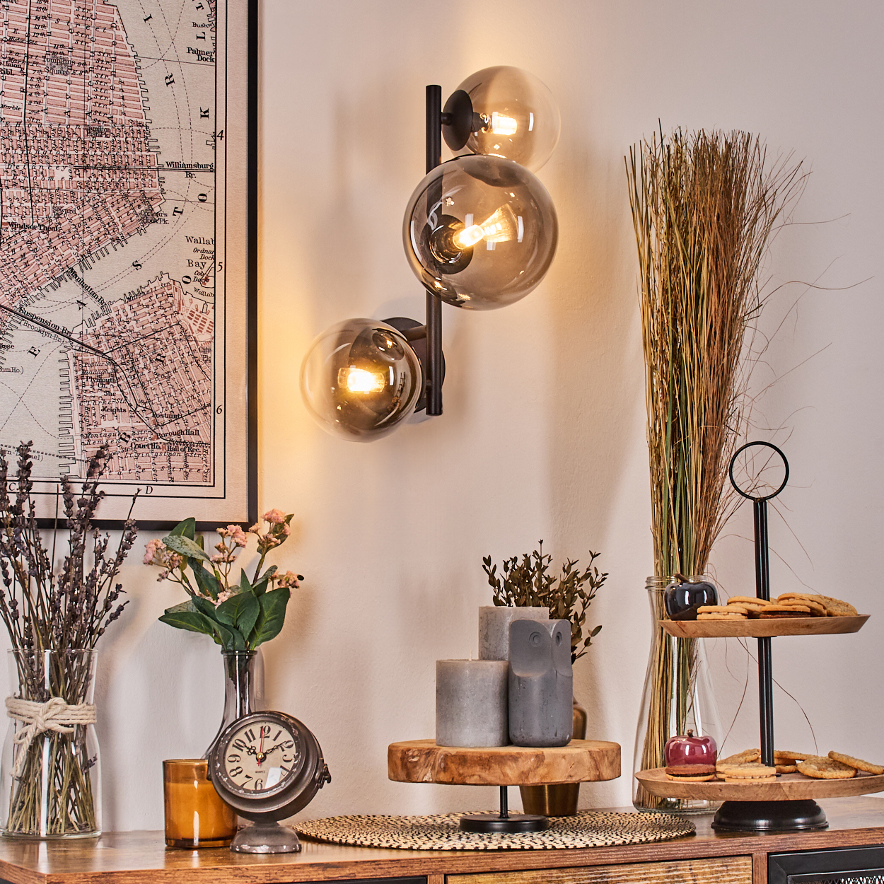Ein Raum mit einer Karte, einer Lampe mit drei Glaskugeln, Blumen, einer Uhr, Kerzen und Keksen auf einem Holzständer.